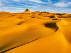 Dunes de sable à perte de vue avec une formation rocheuse à l'horizon.