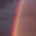 Un arc-en-ciel émerge à travers les nuages sombres, symbolisant un moment de répit et d’espoir après une tempête intérieure.